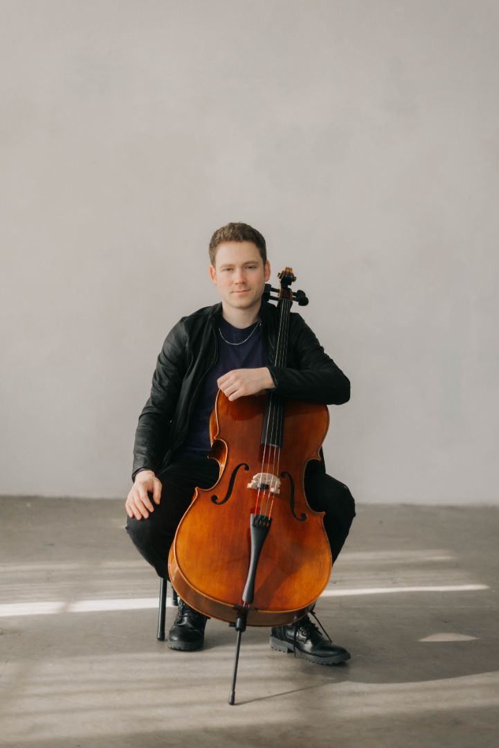 Chris seated with cello in a studio portrait